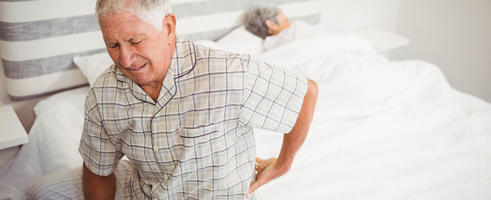 Senior woman suffering from backache sitting on bed in bedroom